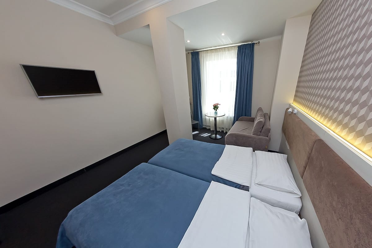 A hotel room with two beds, a TV on the wall, a small table with a vase of flowers, and a window with curtains.