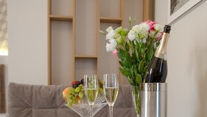 Una mesa con mantel blanco, dos copas de champán, una disposición de frutas y un florero con flores.