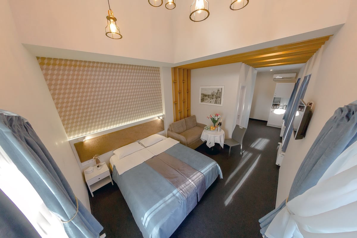A hotel room with a bed, a sofa, a small table with a vase, and a mirror on the wall.