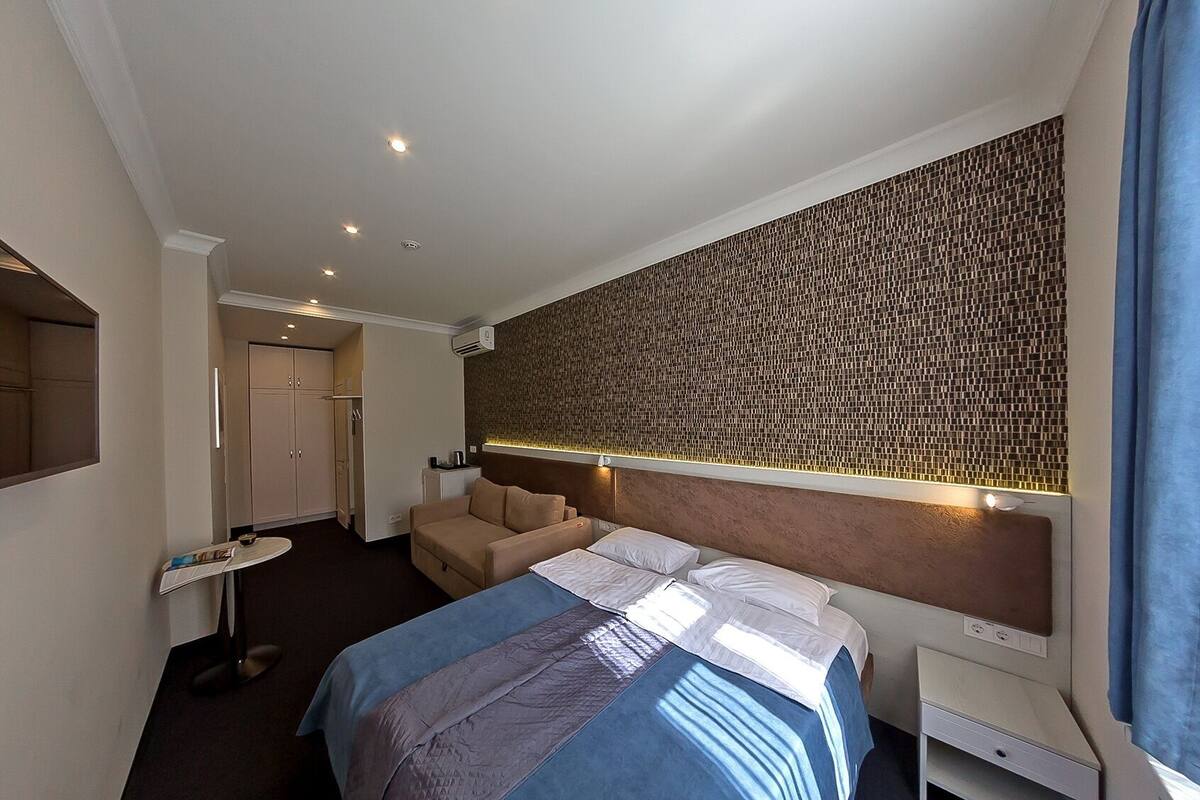 A hotel room with a bed, a desk, a chair, a TV, and a wall with a mosaic pattern.