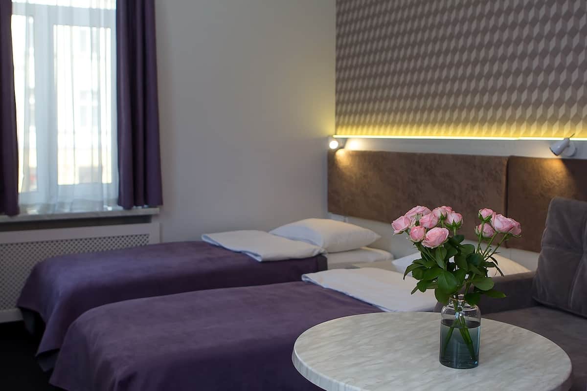 A hotel room with two beds, a round table with a vase of flowers, and a window with curtains.