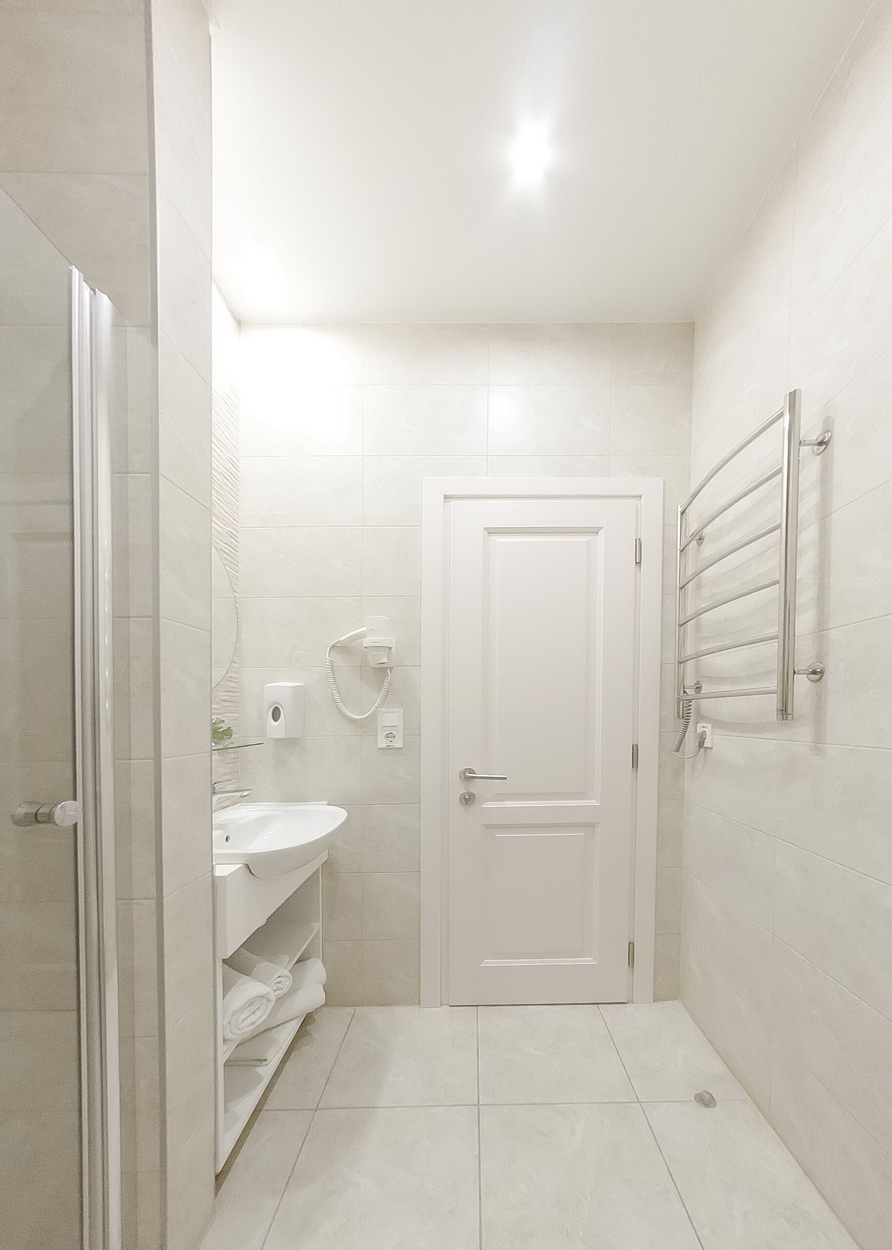 A small, modern bathroom with a glass shower enclosure, a white sink, and a towel rack on the wall.