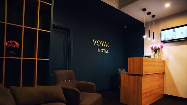 Zona de recepción con pared azul oscuro, mostrador de madera, sofá marrón y una pantalla de televisión que muestra a una mujer.