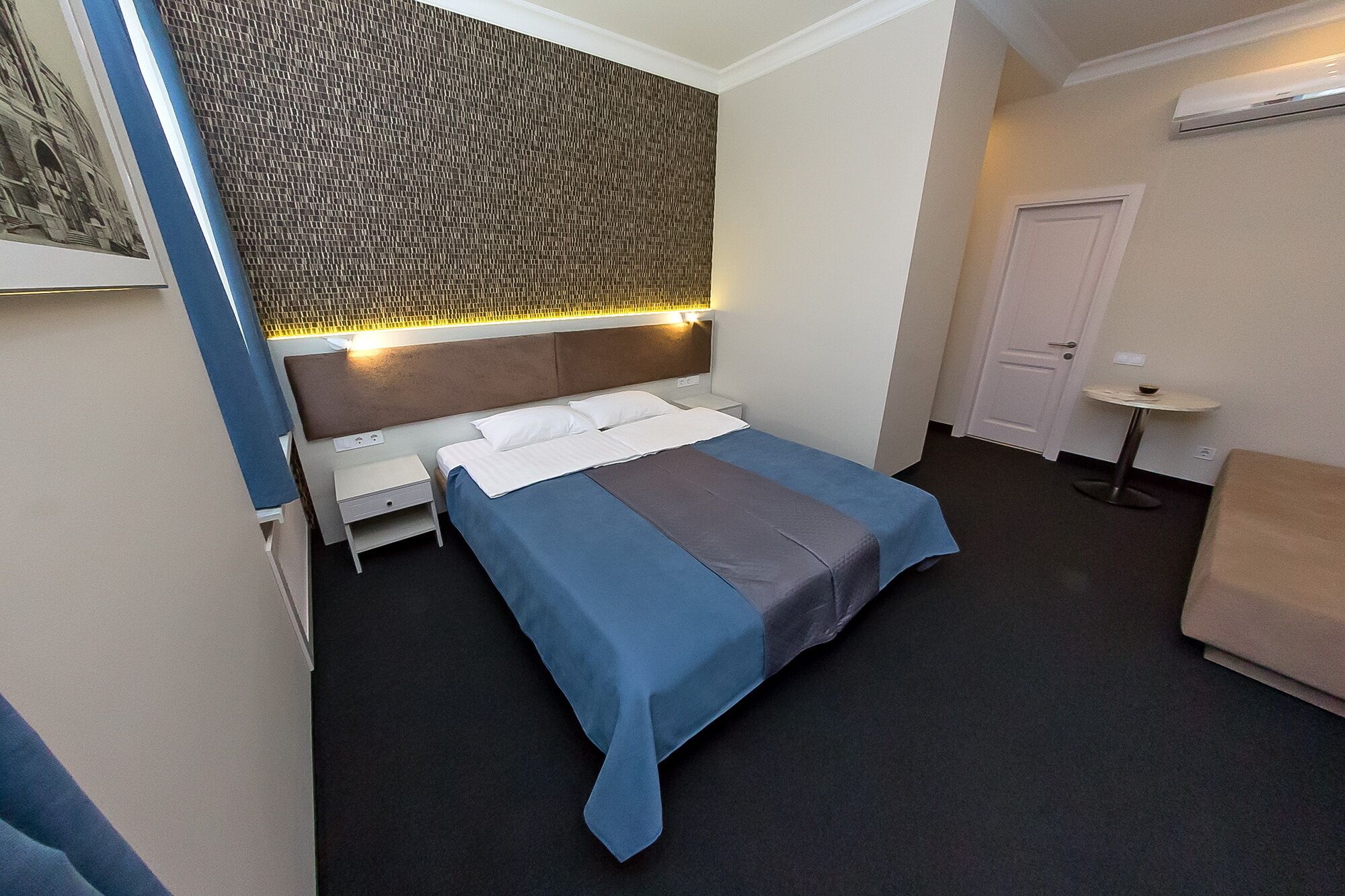 A hotel room with a bed, bedside table, and a small table with a lamp.