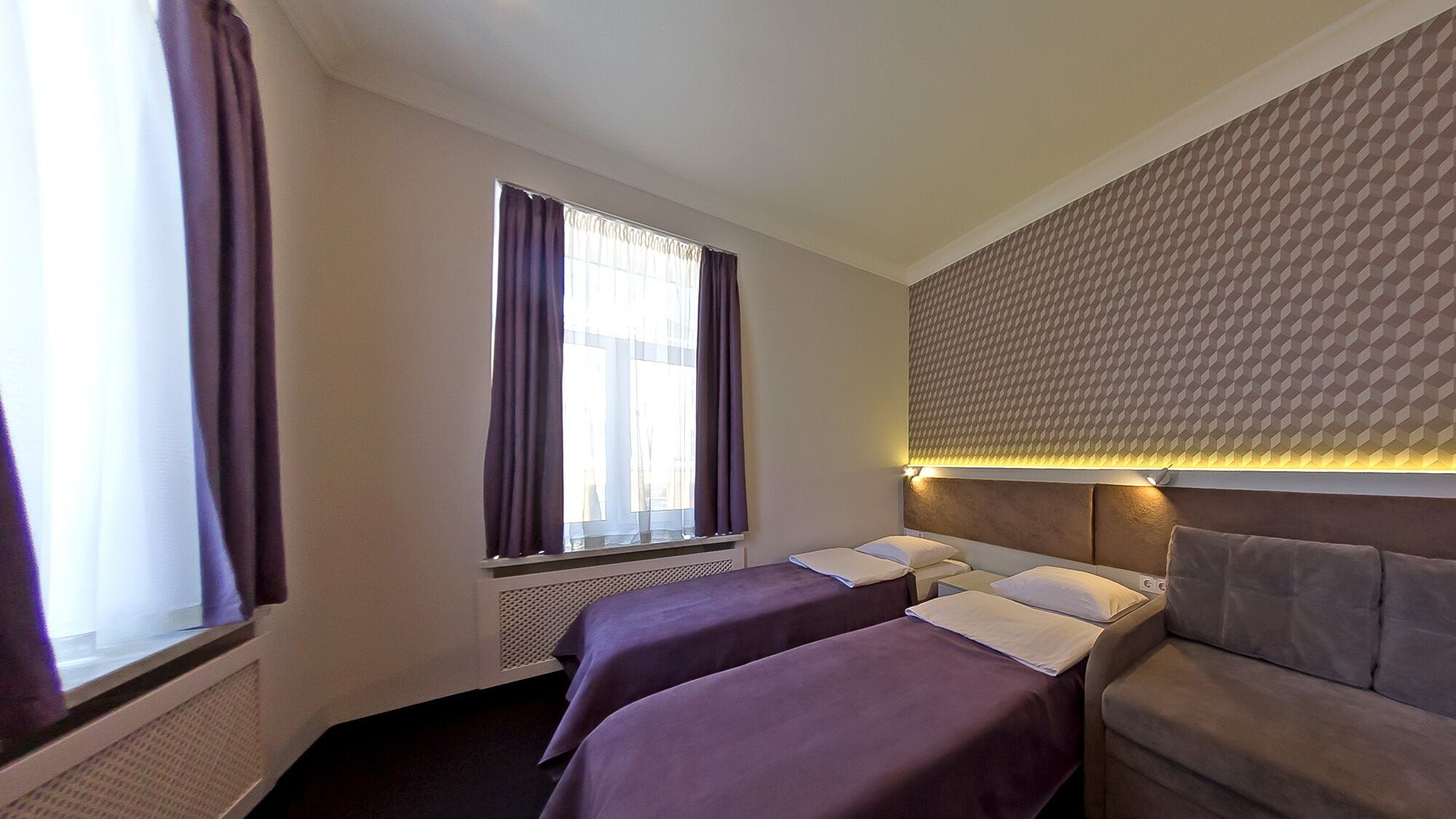 Habitación de hotel con dos camas, ventana con cortinas, pared con estampado y cabecera empotrada con iluminación.