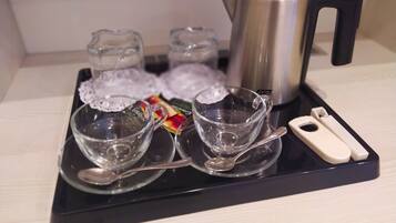 A tray with four clear glass cups, a silver teapot, and a small white device on a black tray.