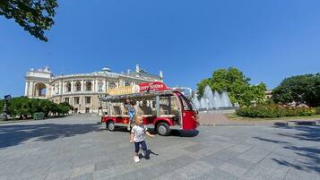 Un niño caminando frente a un autobús turístico rojo, con un edificio al fondo.
