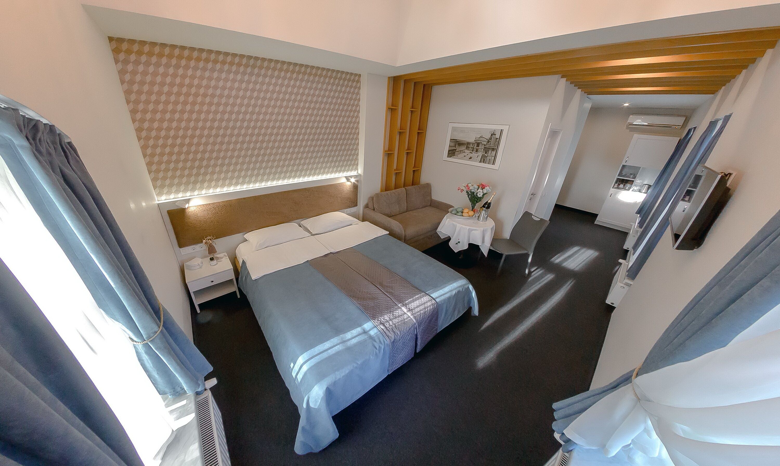 A hotel room with a bed, a sofa, a small table with a vase of flowers, and a picture on the wall.