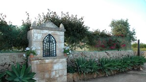 A stone structure with a window, surrounded by plants and a stone wall. - San Domenico Residence (Syracuse)