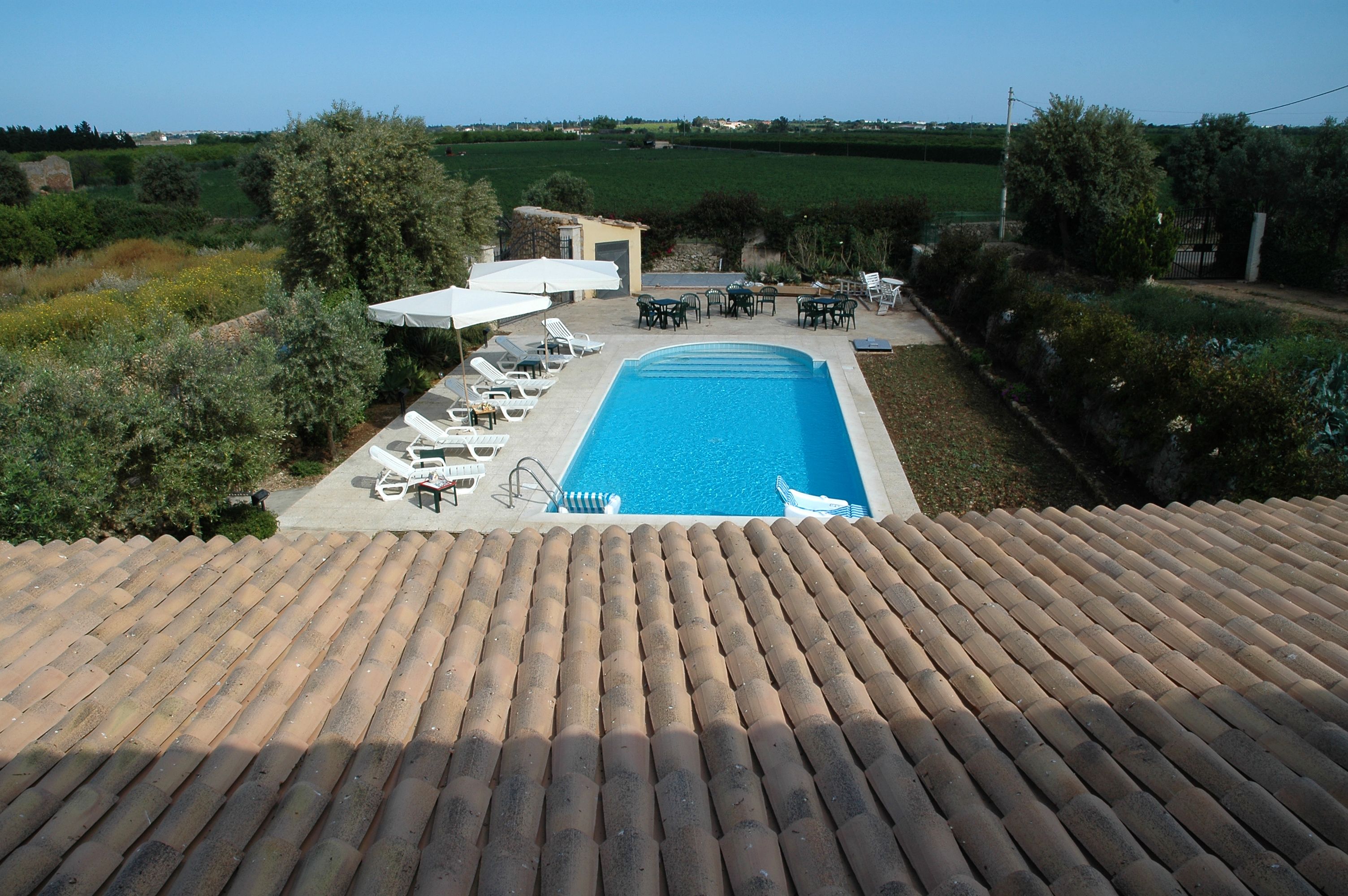 A rooftop pool with a clear view of the surrounding landscape, including a small building and outdoor seating area.