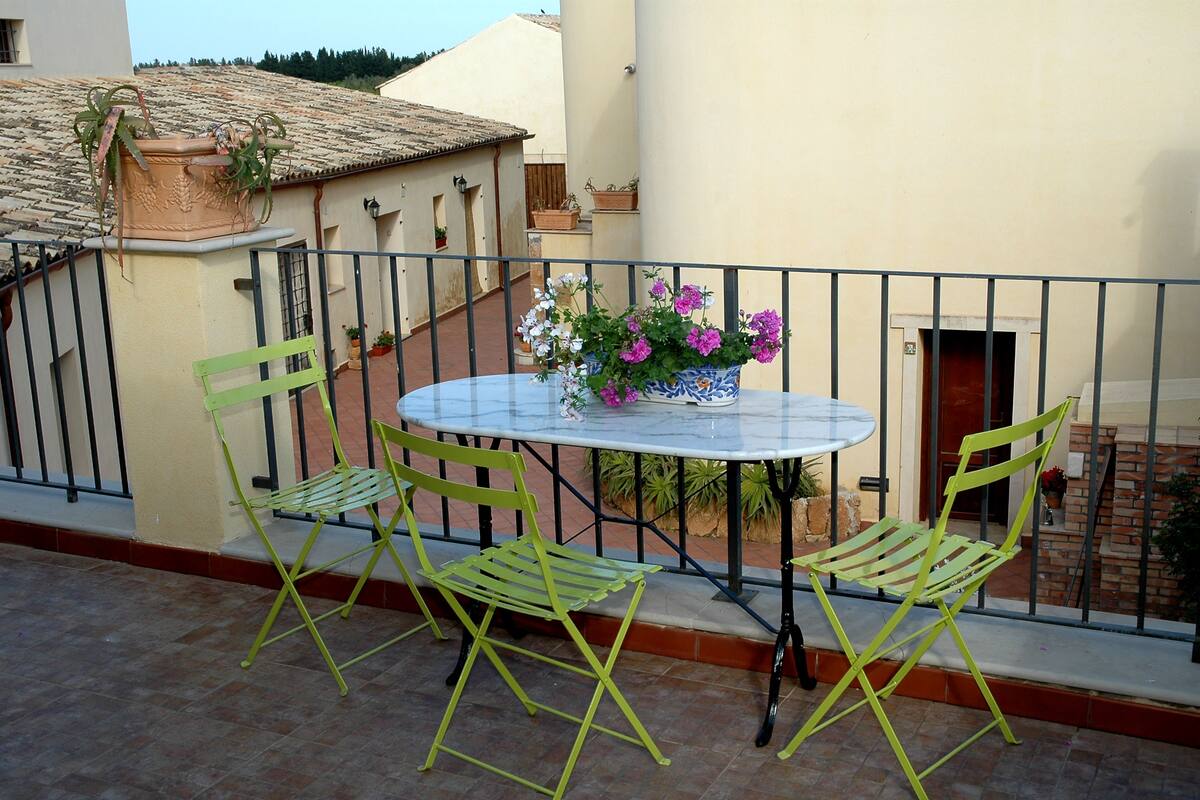 Ein Balkon mit rundem Tisch, zwei Stühlen, einem Blumentopf und einer Blumenvase.