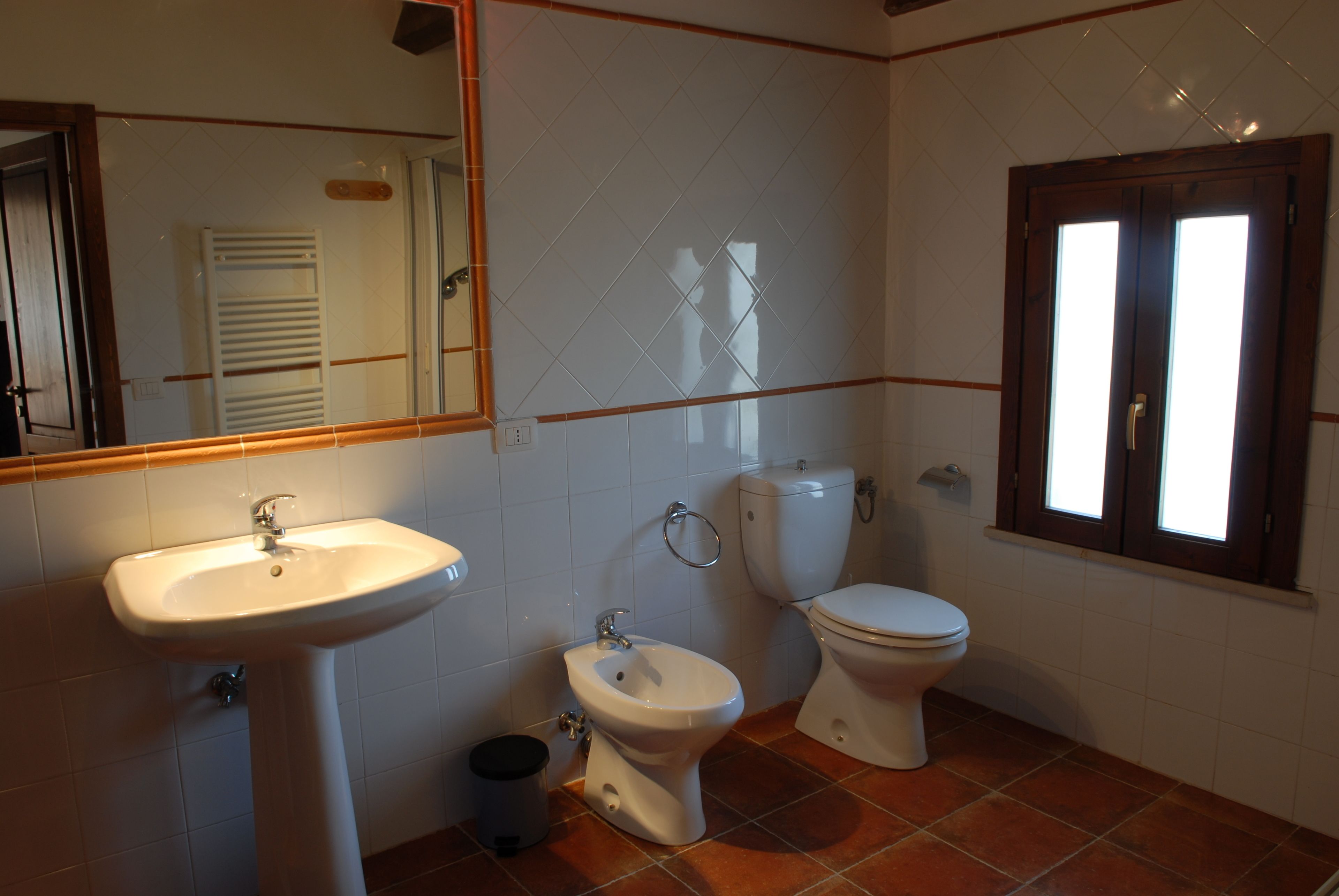 A bathroom with a sink, bidet, toilet, and a window.