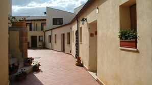 A narrow alleyway with buildings on either side, potted plants, and a tiled floor. - San Domenico Residence (Syracuse)