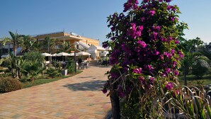 A hotel courtyard with a paved walkway, outdoor seating, and a large building with a balcony. - Calabernardo Resort (Noto)
