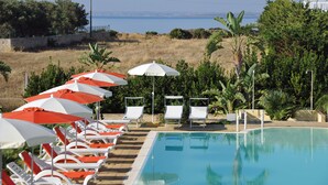 A pool area with sun loungers and umbrellas, surrounded by greenery and a view of the sea. - Calabernardo Resort (Noto)
