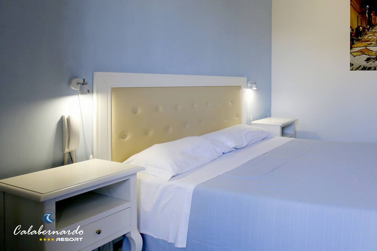 A hotel room with a bed, bedside tables, a telephone, and a wall-mounted artwork.