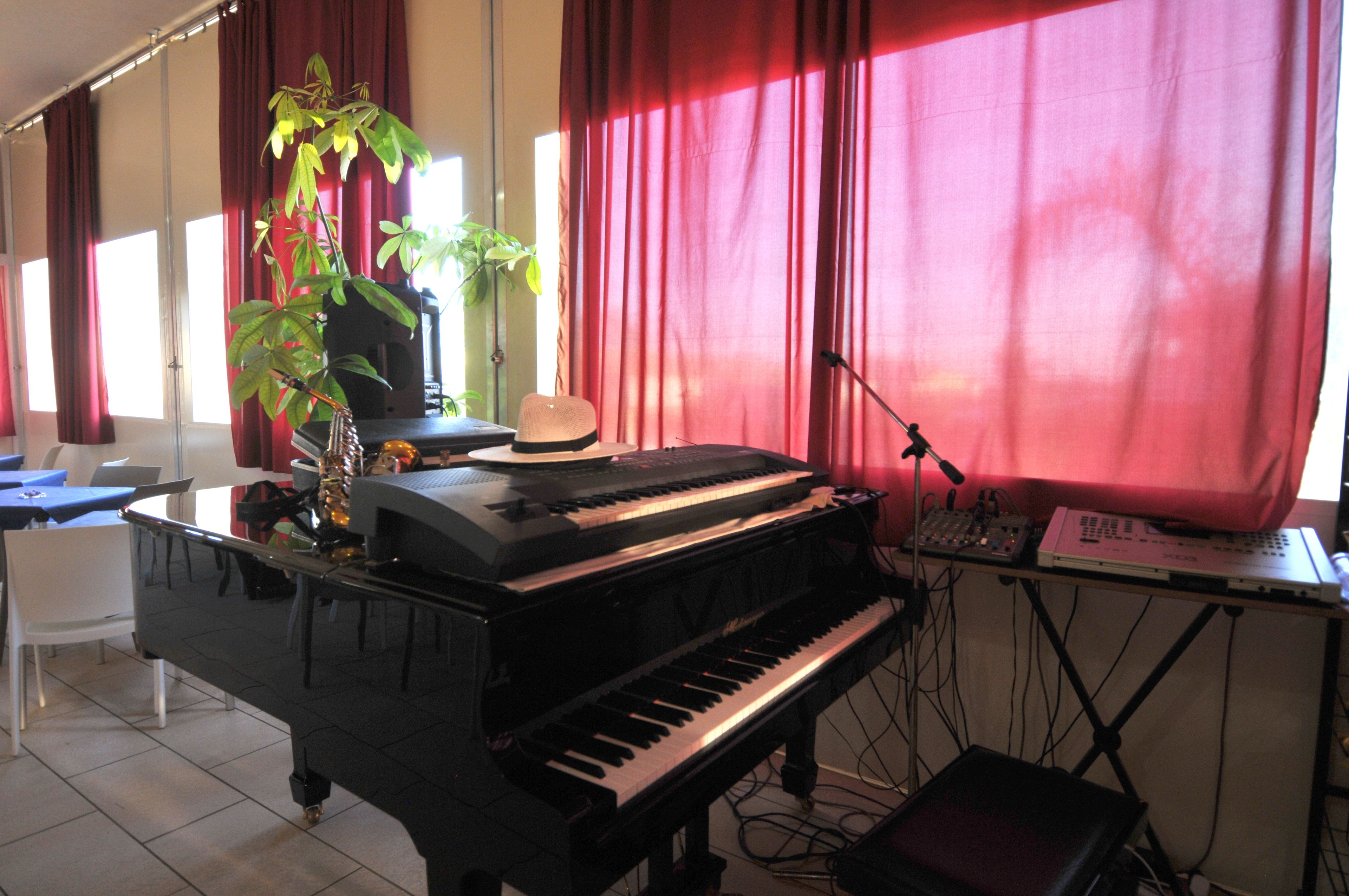 Un pianoforte in una stanza con tende rosse, una pianta e un cappello sul pianoforte.