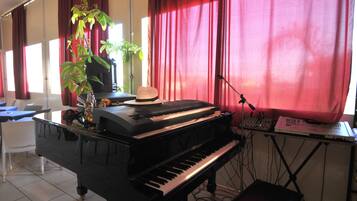 Un pianoforte in una stanza con tende rosse, una pianta e un cappello sul pianoforte.