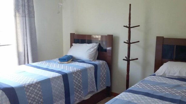 A room with two beds, each with a wooden headboard, a blue and white patterned bedspread, and a white pillow. - Quartos em casa IN Caxias (Duque de Caxias)