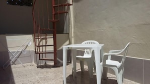 A small outdoor seating area with a white plastic table and two chairs, a metal ladder, and a tiled floor. - Quartos em casa IN Caxias (Duque de Caxias)