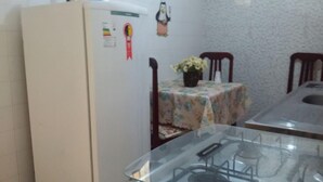 A kitchen with a refrigerator, a table with a floral tablecloth, chairs, and a sink. - Quartos em casa IN Caxias (Duque de Caxias)