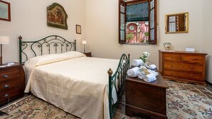 Een slaapkamer met een bed, een dressoir, een nachtkastje, een raam met uitzicht en een spiegel aan de muur.