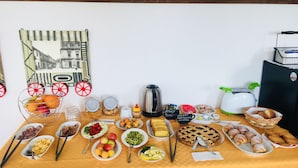 Een tafel met verschillende soorten eten en een waterkoker, voor een witte muur met een lijstwerk afbeelding.