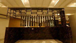 Un interno moderno con una reception in marmo, un divisorio metallico geometrico e una scala con ringhiere in vetro.