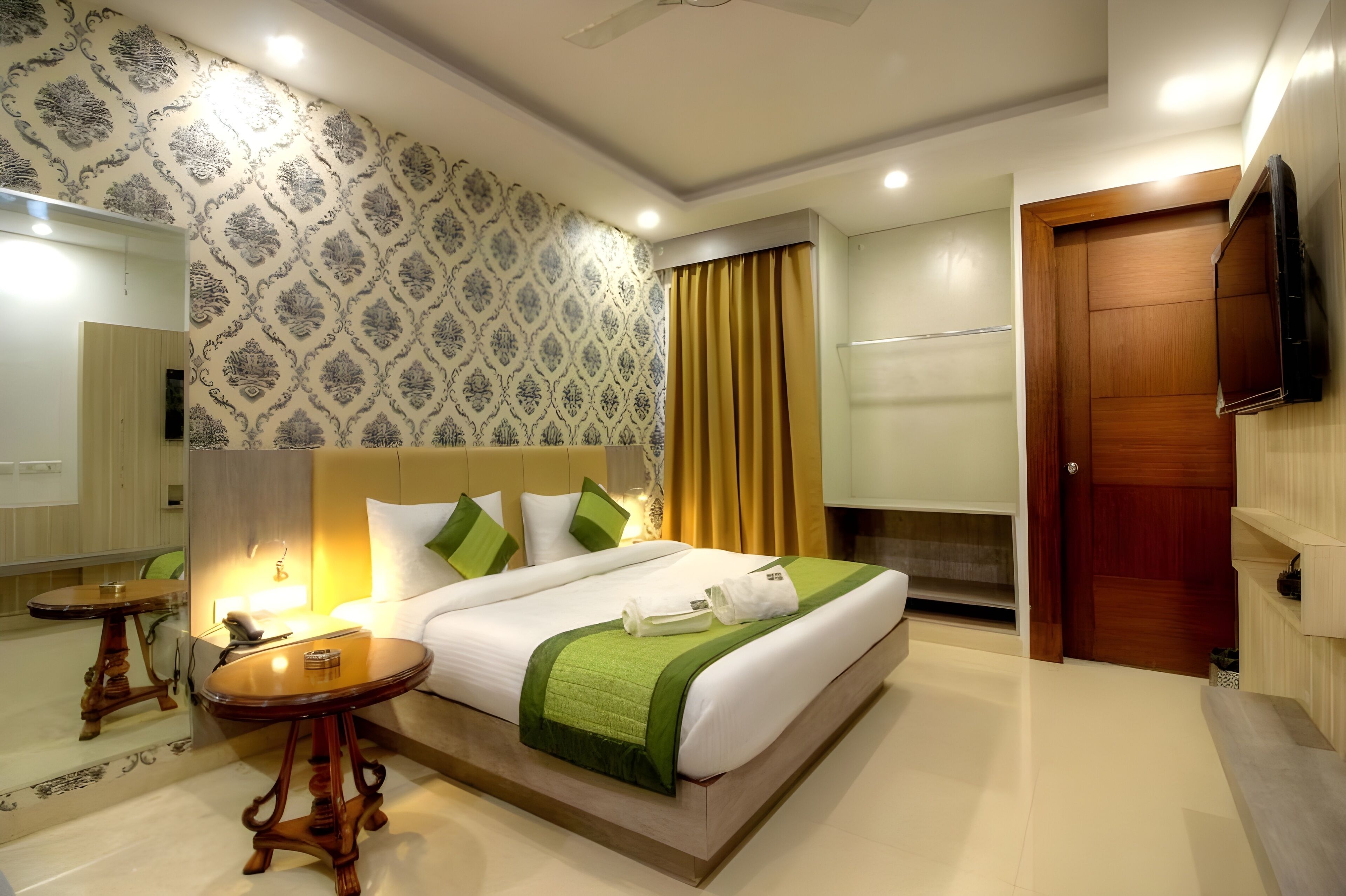 Una habitación de hotel con una cama grande, una mesita de noche, un espejo, un televisor y una puerta de madera.