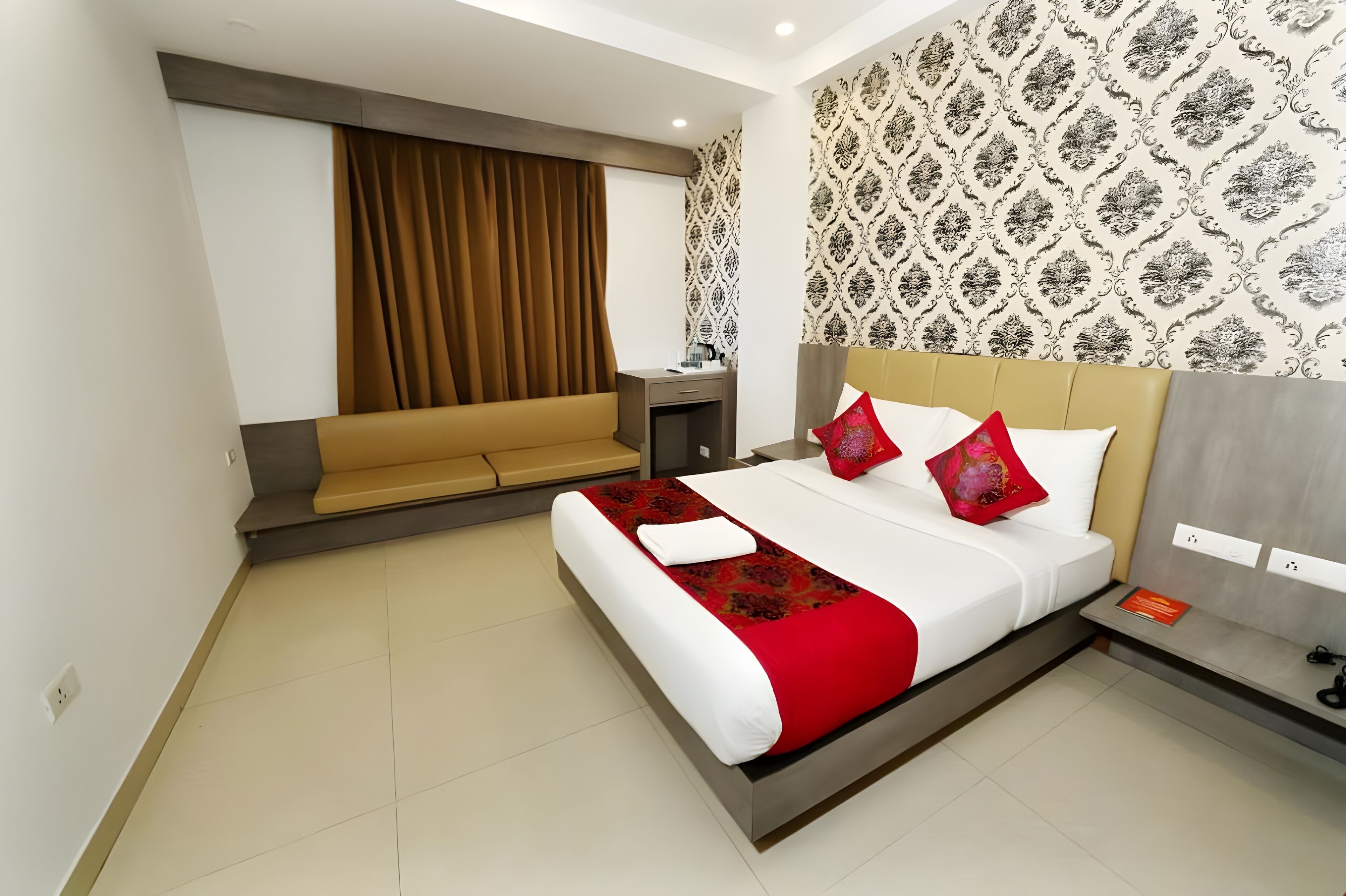 Une chambre d’hôtel avec un lit, une banquette, une table de chevet et un mur décoré d’un motif.
