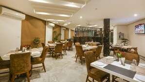 Un ristorante con pavimento in marmo, diversi tavoli con sedie, ventilatori a soffitto e condizionatori d'aria a parete.