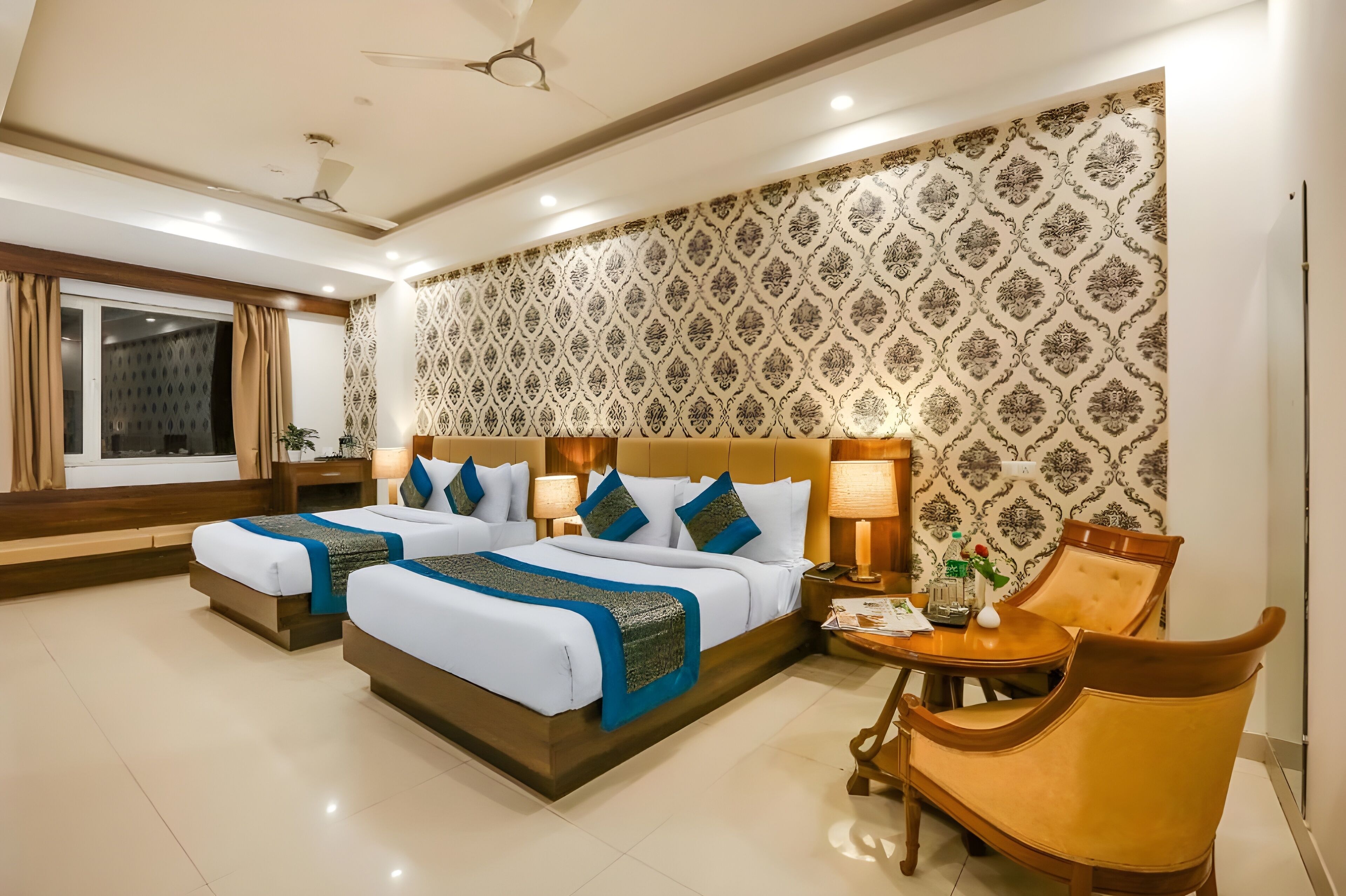 A hotel room with two beds, a sitting area with a chair, a small table, and a decorative wall.