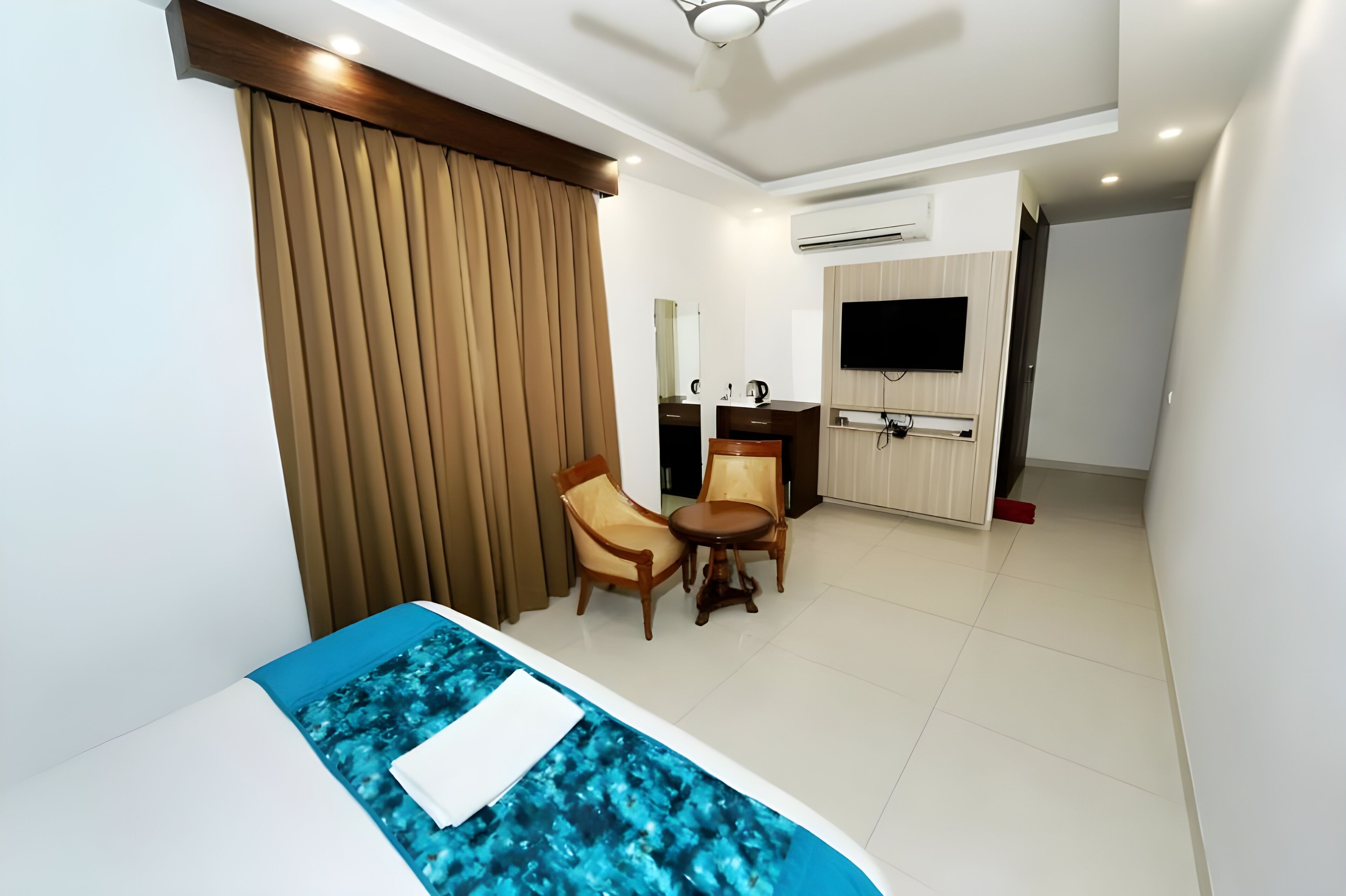 A hotel room with a bed, a desk with chairs, a TV, and an air conditioning unit.