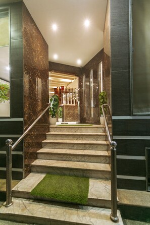 A marble staircase with a metal handrail, leading to a reception area with a plant and a sign. - Hotel Almati Inn (New Delhi)