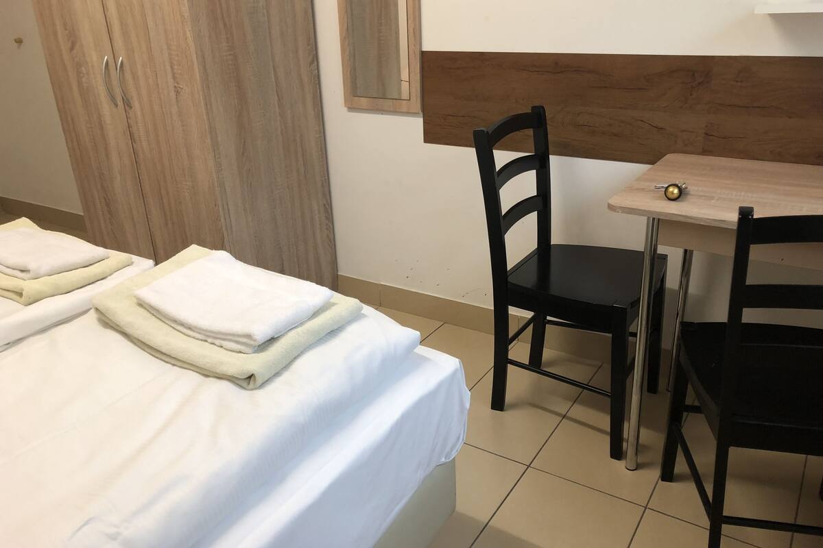 A hotel room with a bed, two chairs, a small table, and a wooden wardrobe.