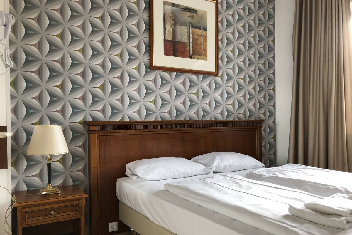 A neatly made bed with white linens, a wooden headboard, and a patterned wall.