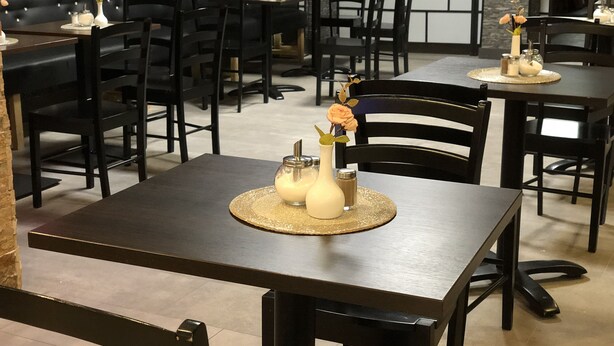 A restaurant with dark wooden tables and chairs, some with flowers and condiments on the table centerpieces. - Hotel Moji (Cologne)