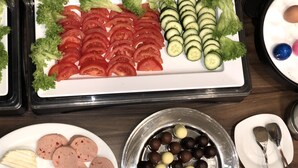 A buffet with sliced tomatoes, cucumbers, and olives on white plates. - Hotel Moji (Cologne)