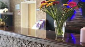 A reception area with a stone wall, a glass vase with flowers, and a framed picture on the wall. - Hotel Moji (Cologne)