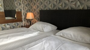 A hotel room with two beds, a nightstand with a lamp, and a wall with a geometric pattern. - Hotel Moji (Cologne)