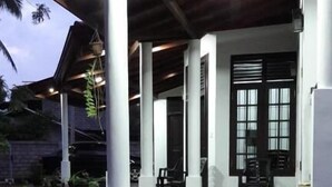 Un espacio al aire libre techado, con columnas blancas, piso de concreto y plantas en macetas.