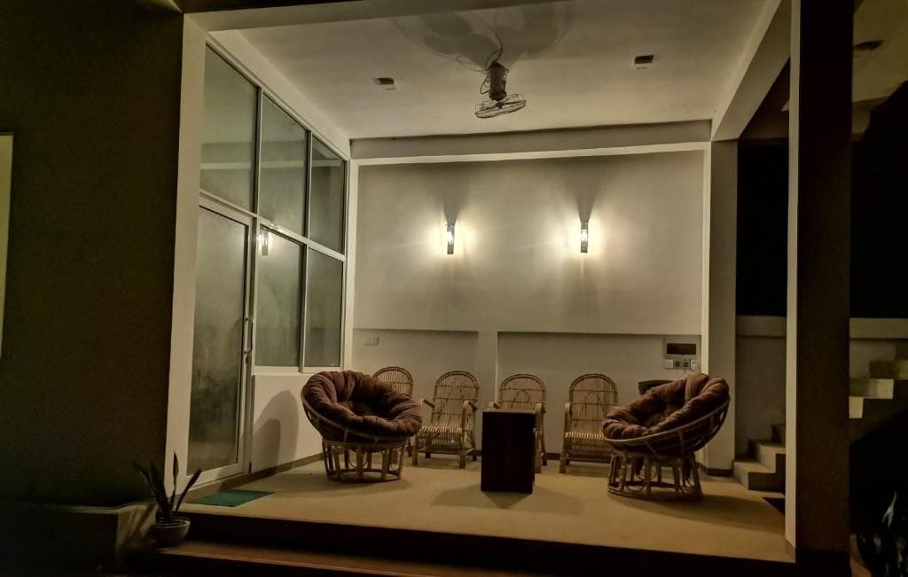 A room with a large window, a ceiling fan, and four wicker chairs arranged around a central table.