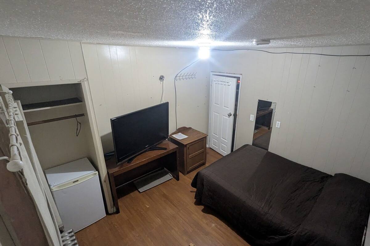 Una habitación compacta con cama, escritorio con computadora, refrigerador pequeño y armario.