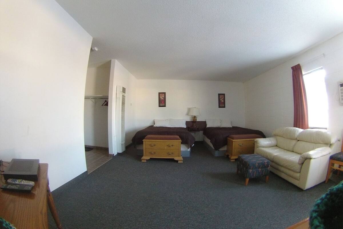 Una habitación con dos camas, un sofá, una mesita y una ventana con cortinas.