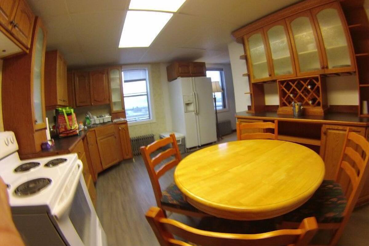 Cocina compacta con armarios de madera, estufa blanca, mesa de comedor con sillas y refrigerador.