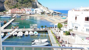 A coastal marina with boats docked, a promenade with outdoor seating, and buildings with balconies overlooking the water.