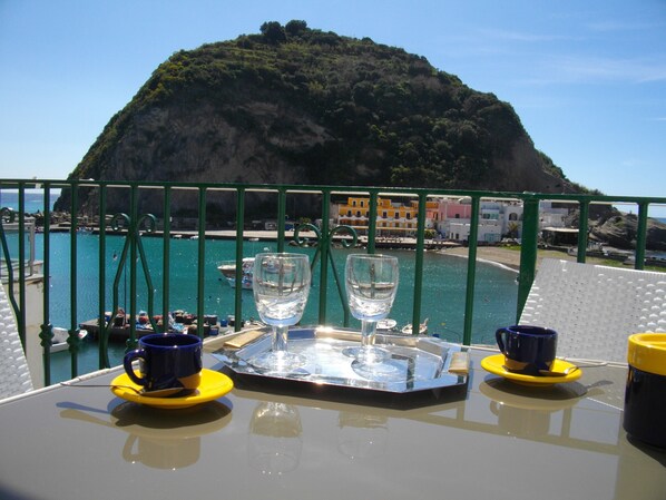 A table with two glasses and two cups on a tray, overlooking a coastal area with boats and buildings.