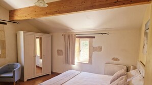 A bedroom with a bed, a chair, a wardrobe, a window, and a radiator. - Le Moulin charming cottage near St Emilion (Lugaignac)