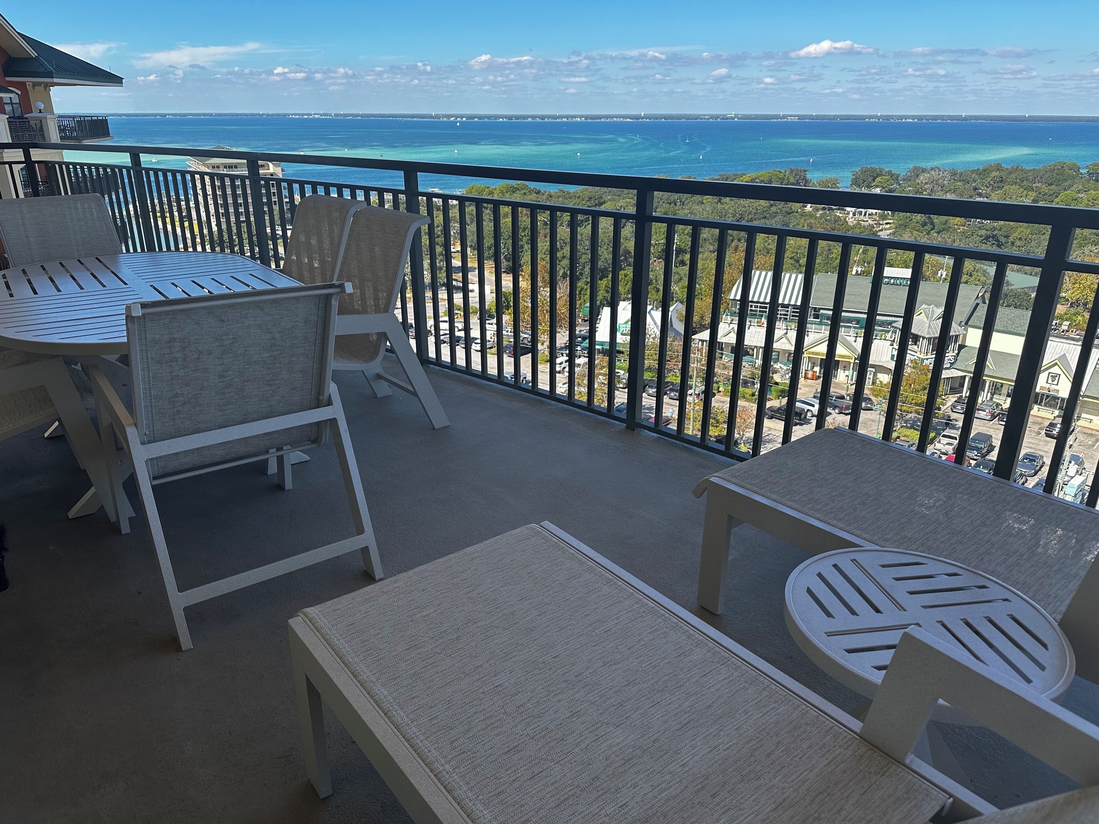 A balcony with a table and chairs, overlooking a coastal view with the ocean and a distant shoreline.