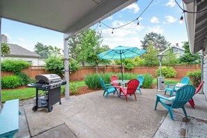 An outdoor patio with a grill, chairs, and an umbrella.